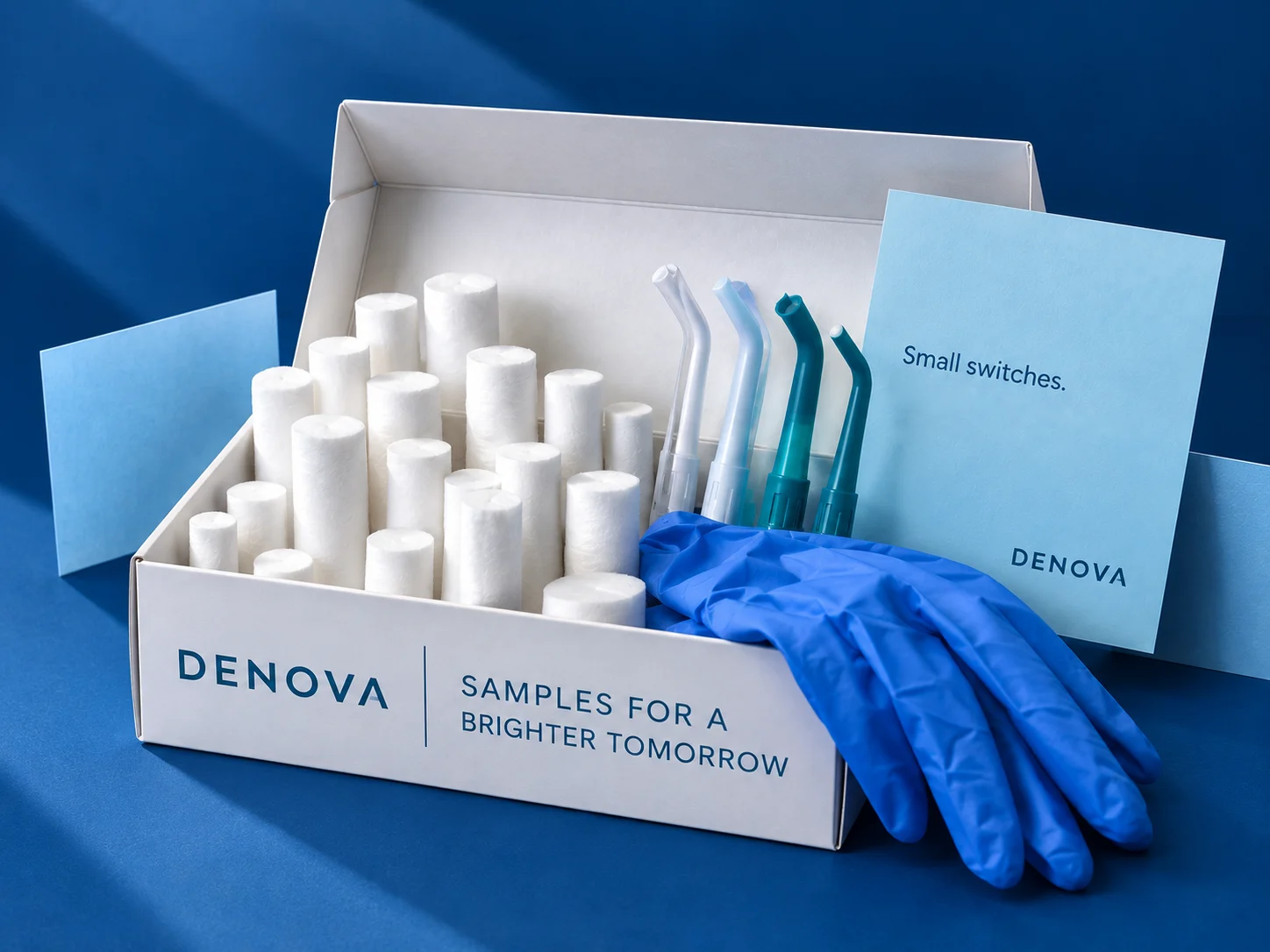 An open DENOVA sample box holding cotton rolls and suction tips, with a nitrile glove resting against it and two blue cards behind.